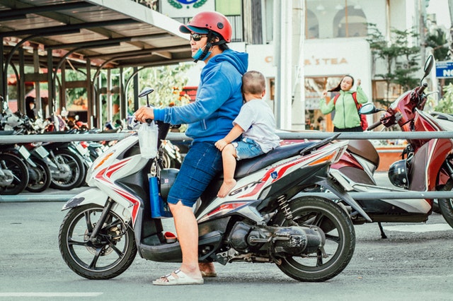 Muž s dieťaťom na motorke stojí uprostred rušnej ulice.jpg