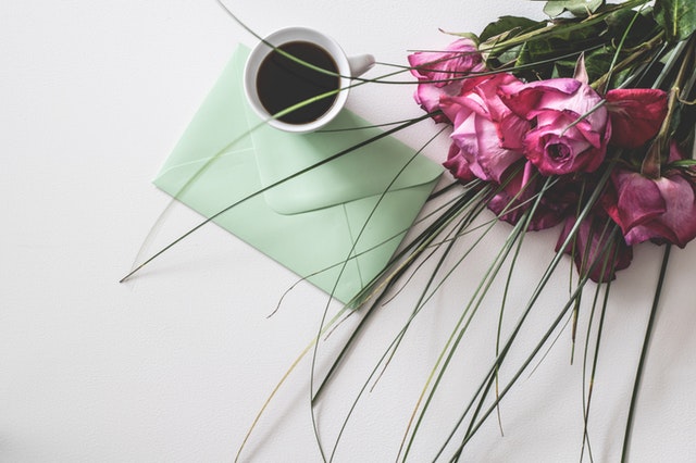 Svetlozelená obálka na stole, šálka kávy a kytica kvetov.jpg